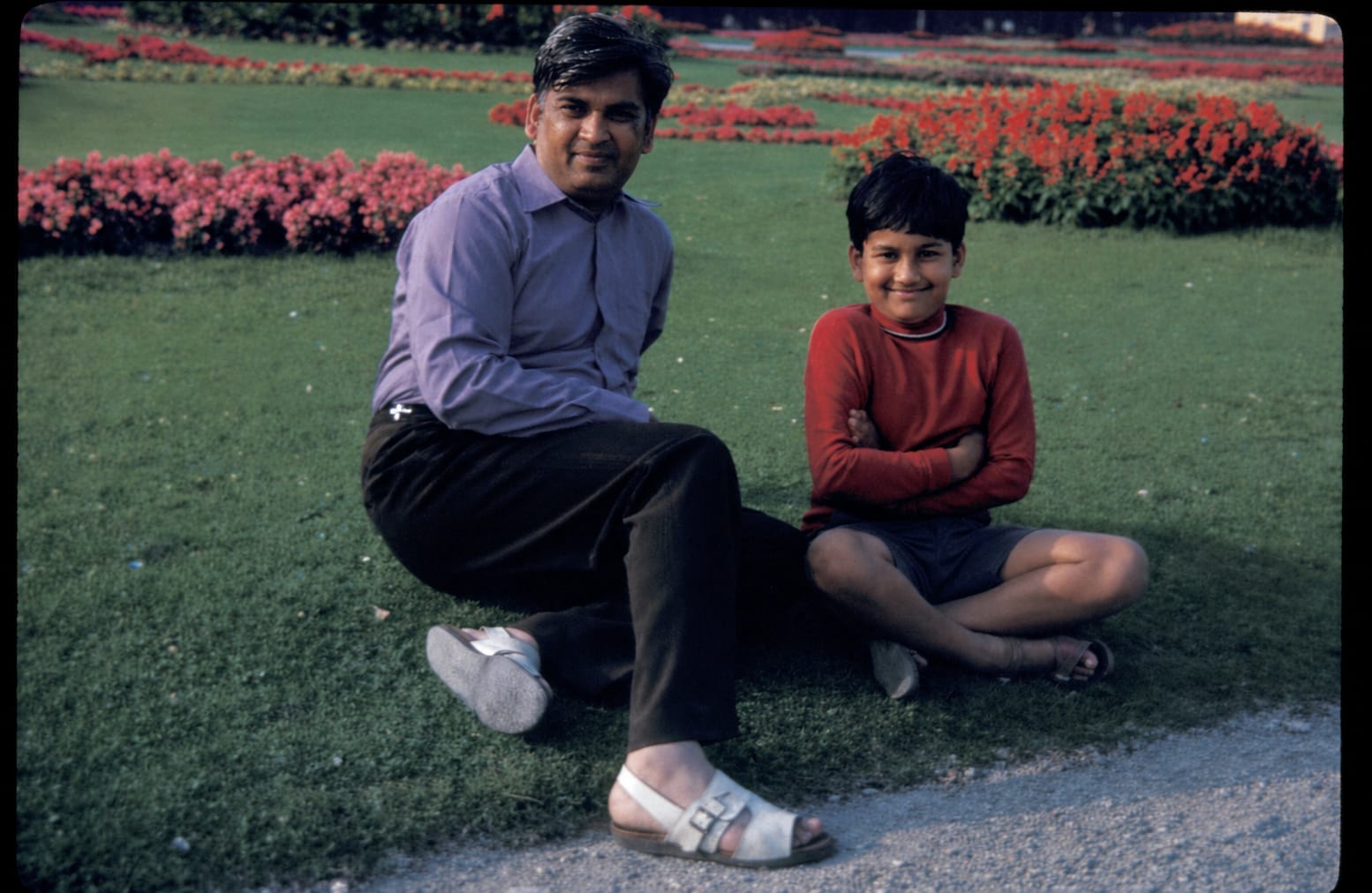 Ram Prashad Gupta sitting on the grass with young Sunil in a formal flower garden