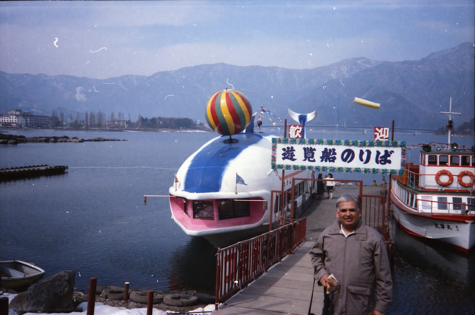 Ram Prashad Gupta by a large pleasure boat at a lake in Japan with snowy mountains behind