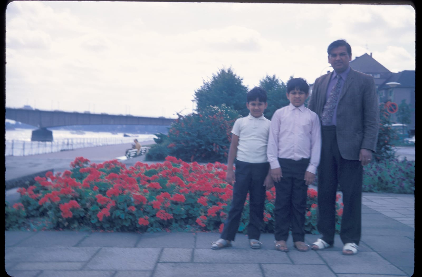 Ram Prashad Gupta with his two sons by a riverside with a bridge behind