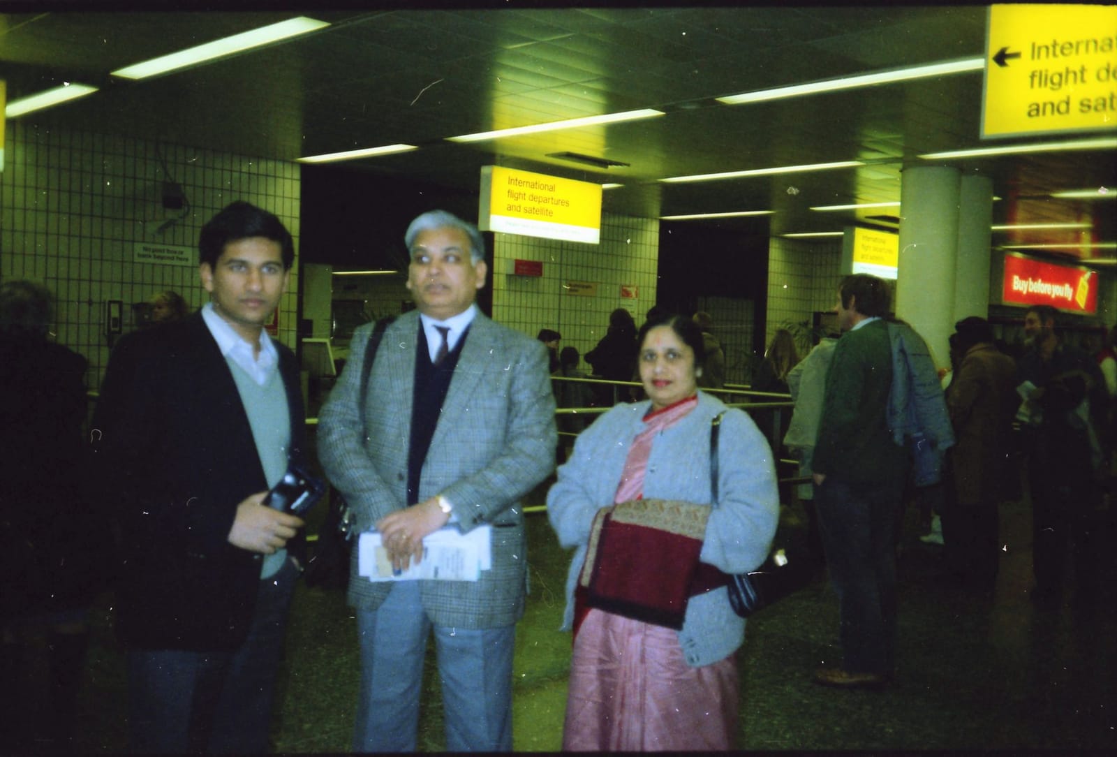Sunil with his father and mother under an airport departures sign, 1980s