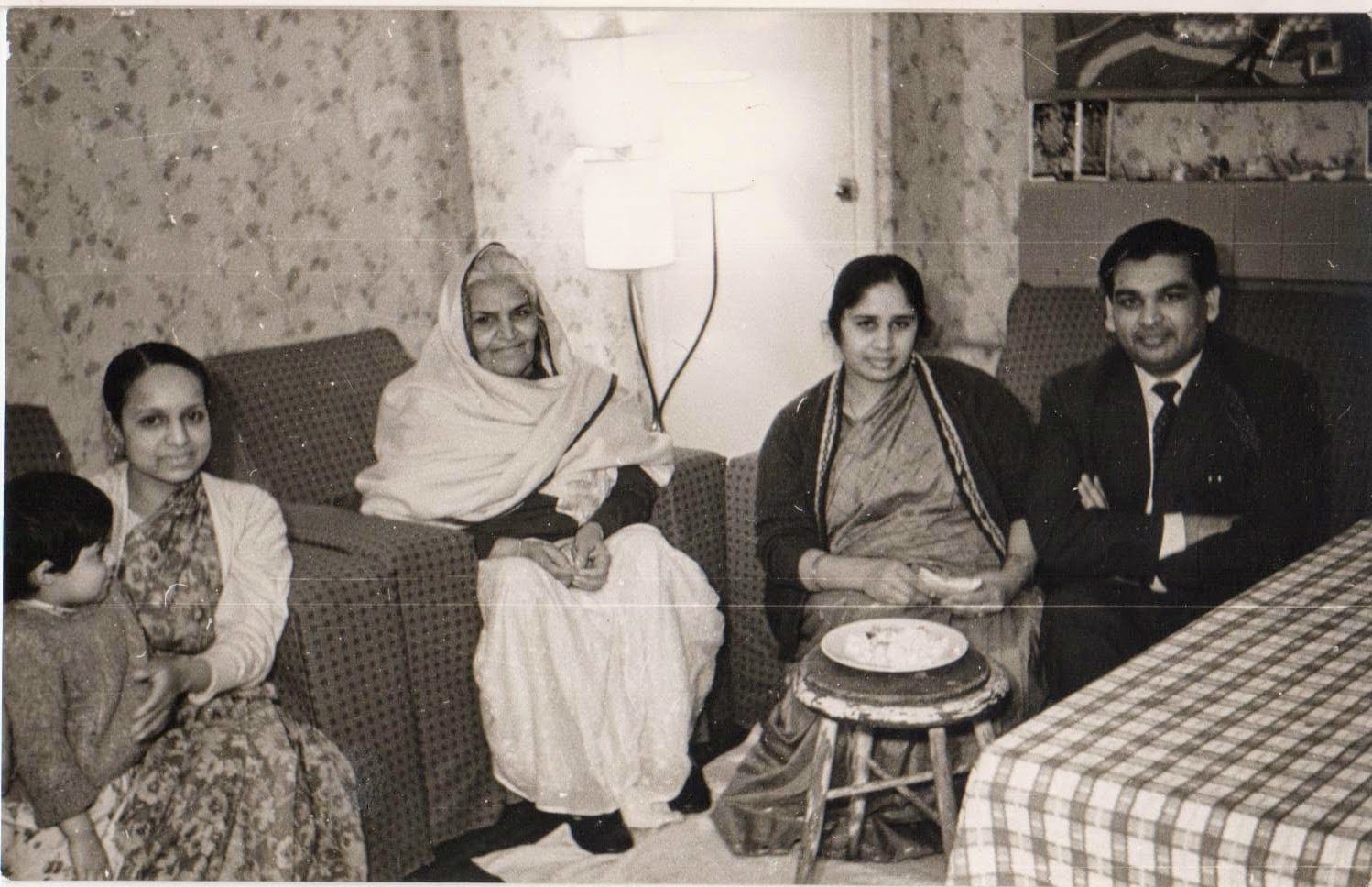 Indian family gathered on a sofa in an English front room, black and white