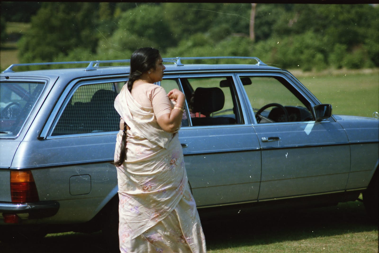 Sunil's mother in a sari beside a blue Mercedes estate car in England, 1980s