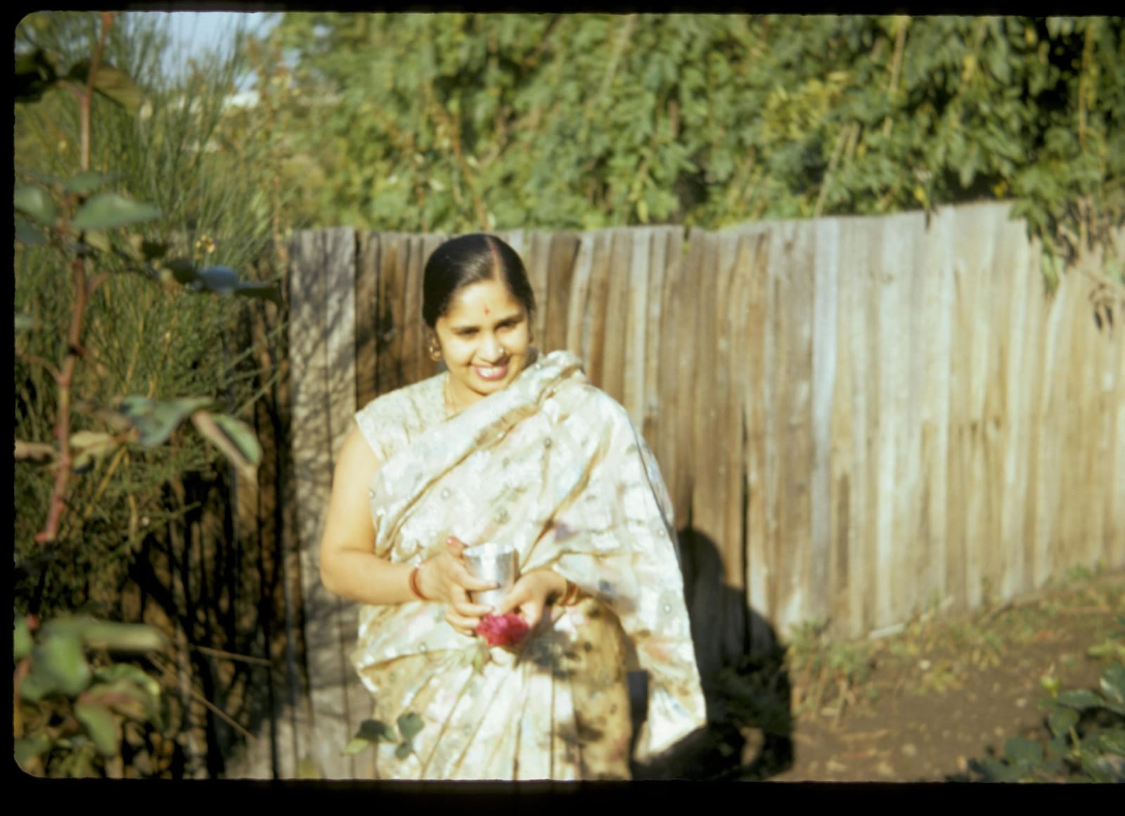 Sunil's mother as a young woman in a sari holding a rose in a garden