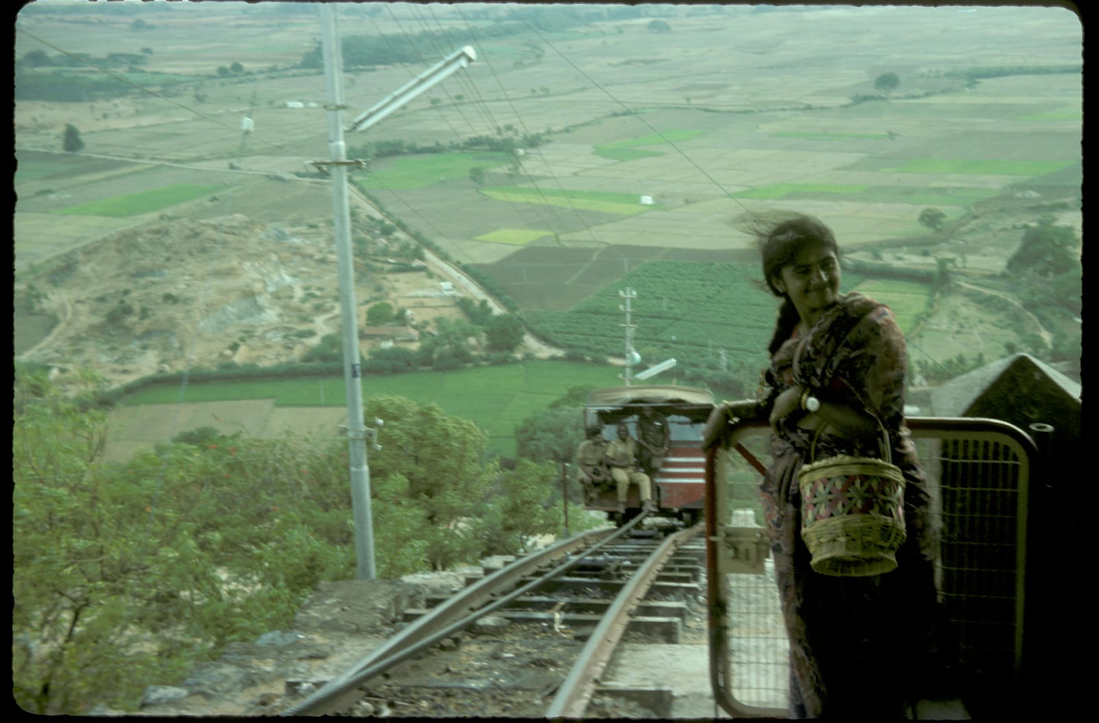 Sunil's aunt with a basket on a mountain railway in India, green valley behind