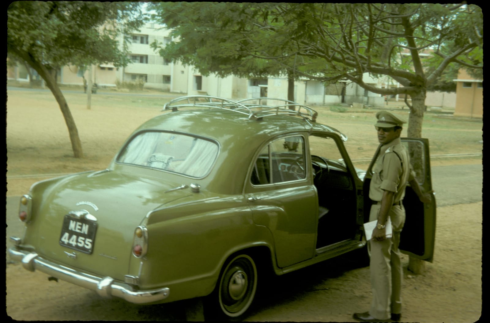 Raj Kumar in officer's uniform beside a classic Hindustan Ambassador car in India